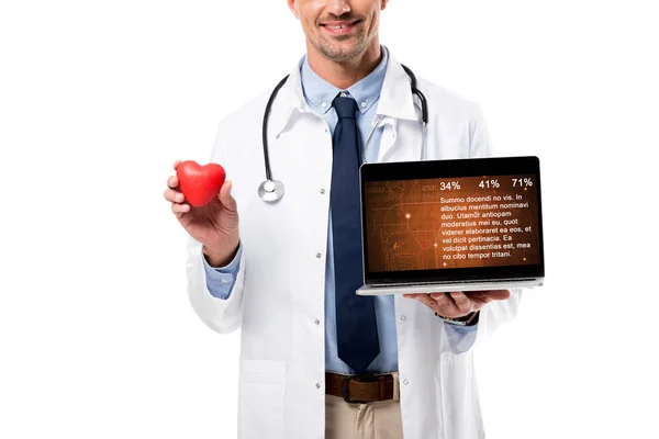 Vista parcial del médico sosteniendo el modelo de corazón y el ordenador portátil con datos de salud en la pantalla aislada en blanco, concepto de salud del corazón - foto de stock