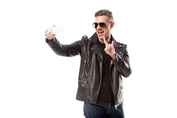 Eccitato uomo adulto in occhiali da sole mostrando segno di roccia e prendendo selfie su smartphone isolato su bianco — Foto stock