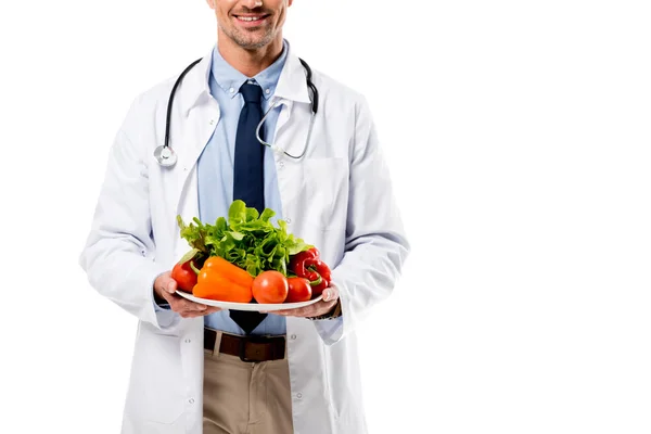 Abgeschnittene Ansicht des Arztes, der Teller mit frischem Gemüse hält, mit Grün isoliert auf weißem, gesundem Ernährungskonzept — Stockfoto