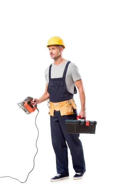 Trabajador de la construcción que sostiene la caja de herramientas y la sierra eléctrica aislada en blanco - foto de stock