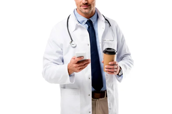 Vista cortada de médico segurando café para ir e usando smartphone isolado no branco — Fotografia de Stock