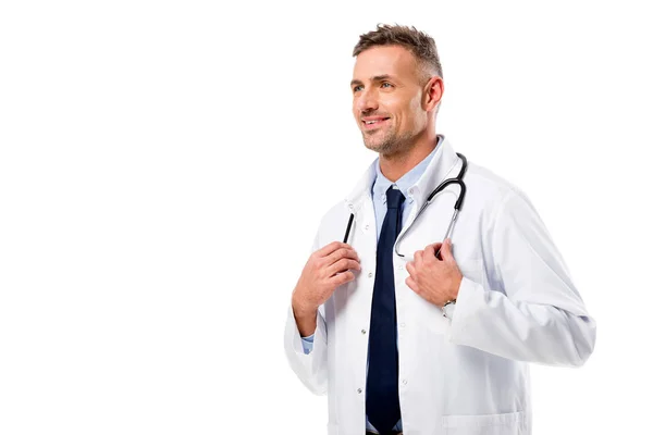Guapo doctor en bata blanca con estetoscopio mirando hacia otro lado aislado en blanco - foto de stock