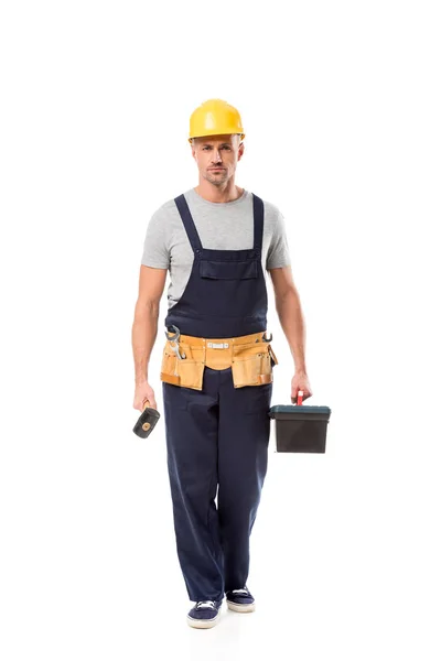 Trabajador de la construcción sosteniendo martillo, caja de herramientas y mirando a la cámara aislada en blanco - foto de stock