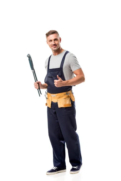 Sonriente trabajador sosteniendo la llave de tubo y haciendo pulgar hacia arriba signo aislado en blanco - foto de stock