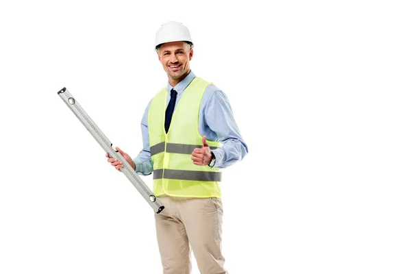 Sonriente ingeniero sosteniendo el nivel de espíritu y mostrando el pulgar hacia arriba aislado en blanco - foto de stock