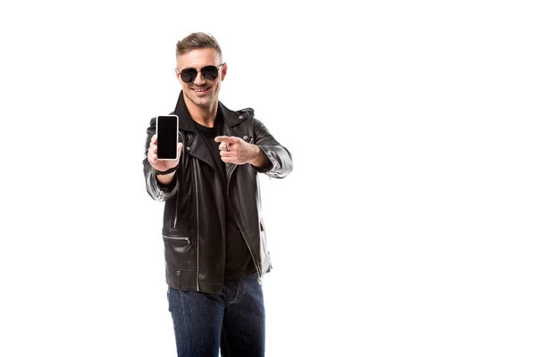 Homem adulto elegante em jaqueta de couro apontando com o dedo para o smartphone com tela em branco isolada no branco — Fotografia de Stock