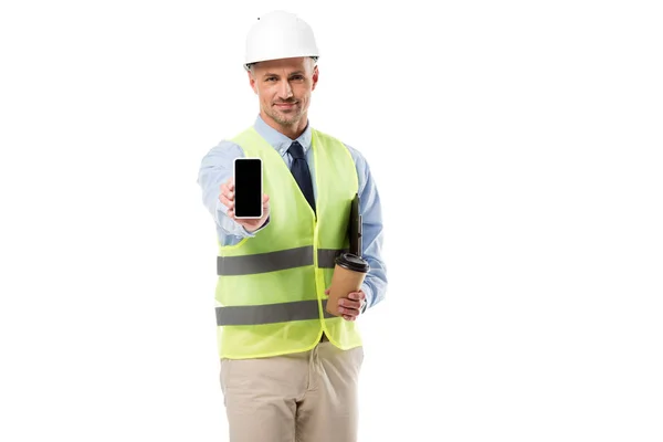 Ingeniero guapo sosteniendo teléfono inteligente con pantalla en blanco y café para ir aislado en blanco - foto de stock