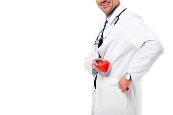 Обрізаний вид усміхненого лікаря в білому пальто зі стетоскопом, що тримає модель серця в руці ізольовано на білому, концепція охорони здоров'я — стокове фото