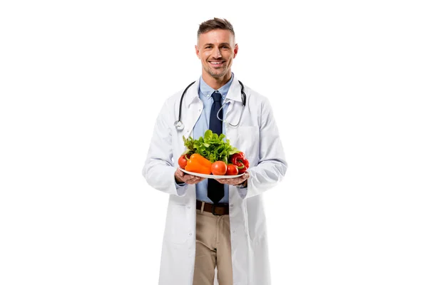Arzt blickt in die Kamera und hält Teller mit frischem Gemüse isoliert auf weißem, gesundem Ernährungskonzept — Stockfoto