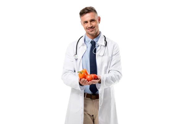 Smiling doctor looking at camera and holding vegetables in hands isolated on white, healthy eating concept — Stock Photo