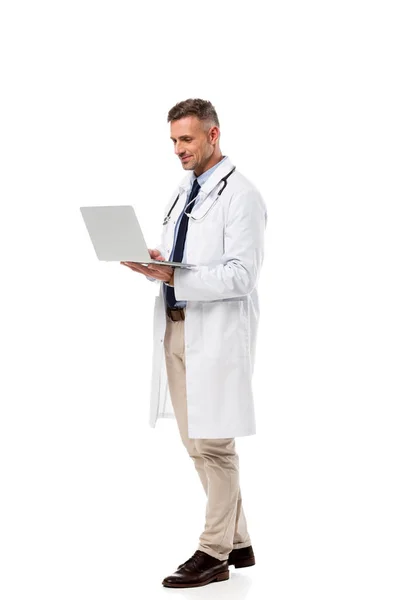 Beau médecin en manteau blanc avec stéthoscope en utilisant un ordinateur portable isolé sur blanc — Photo de stock