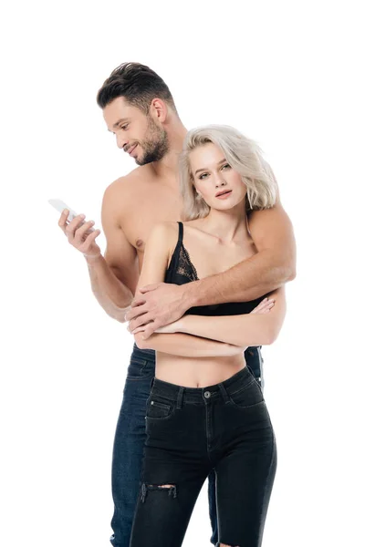 Hombre guapo usando teléfono inteligente, mientras que la hermosa mujer seductora mirando a la cámara aislada en blanco - foto de stock
