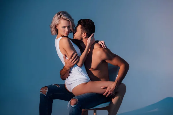 Passionate heterosexual couple sitting on chair and hugging on dark blue background — Stock Photo