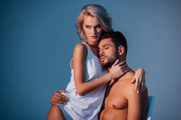 Atractiva mujer y hombre abrazando y mirando hacia otro lado sobre fondo azul oscuro - foto de stock