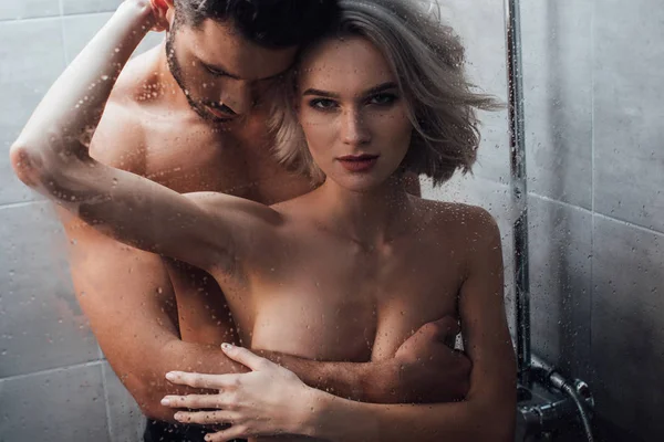 Schöne Frau blickt in die Kamera und umarmt Mann beim Duschen — Stockfoto