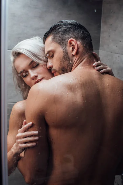 Joven pareja apasionada abrazos y besos mientras toma ducha juntos - foto de stock
