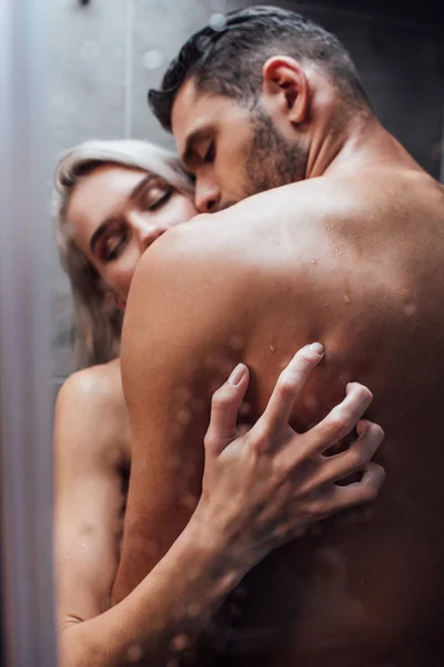 Избирательный фокус страстной обнаженной гетеросексуальной пары, обнимающей и целующейся во время принятия душа вместе — стоковое фото