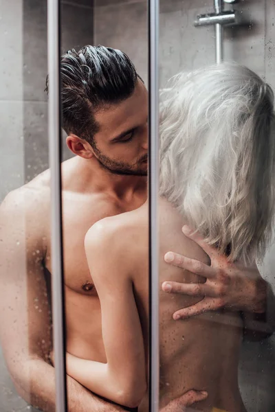 Beautiful naked couple hugging and kissing in passion while taking shower together — Stock Photo