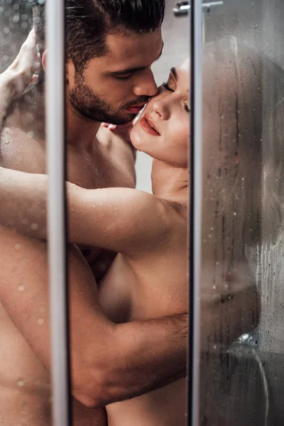 Apasionada pareja desnuda abrazos y besos mientras toman ducha juntos - foto de stock