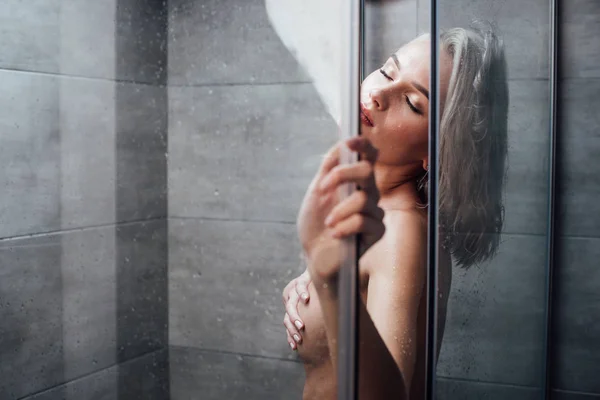 Belle jeune femme nue avec les yeux fermés tenant porte de douche et posant dans la salle de bain — Photo de stock