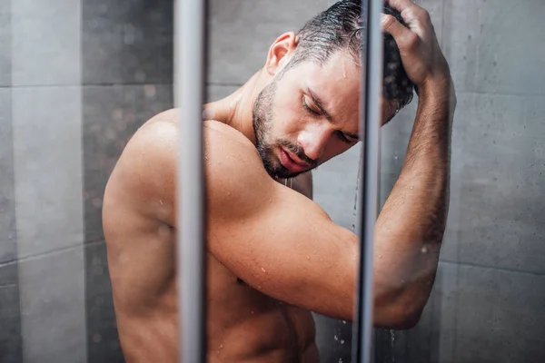 Enfoque selectivo de hombre guapo con los ojos cerrados tomando ducha en el baño - foto de stock