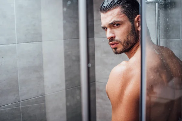 Bel homme regardant la caméra tout en prenant une douche dans la salle de bain — Photo de stock