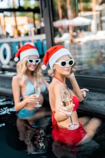 Красивые женщины в шляпах Санта-Клауса с бокалами шампанского, отдыхающие в бассейне, новая концепция празднования года — стоковое фото