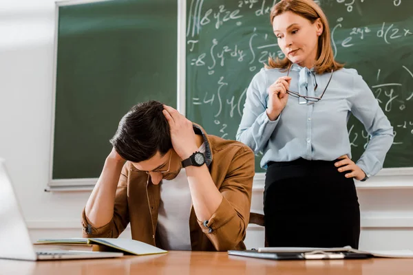 Étudiant tenant la tête et regardant bouleversé près enseignante — Photo de stock