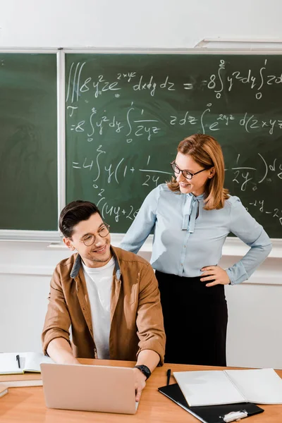 Profesora mirando a una joven estudiante y sonriendo en el aula - foto de stock