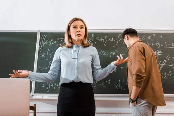 Profesora haciendo gestos en el aula en ropa formal cerca de la estudiante - foto de stock