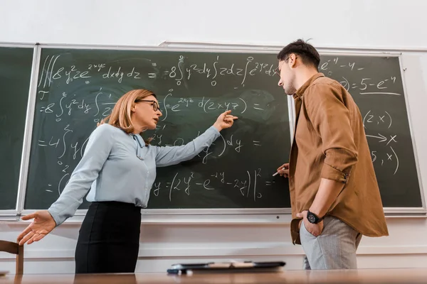 Female professor pointing at equations to student in classroom — Stock Photo