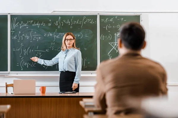 Profesor señalando ecuaciones en el aula con el estudiante - foto de stock