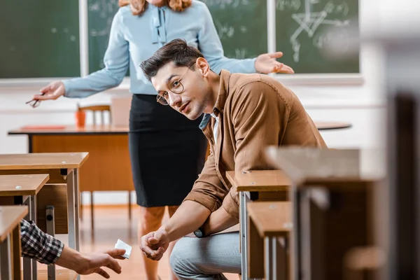 Foco seletivo de professora insatisfeita olhando para estudante do sexo masculino tomando berço durante exame em sala de aula — Fotografia de Stock