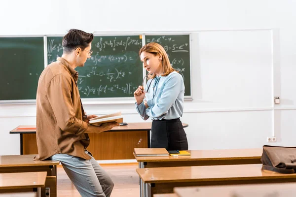 Männlicher Schüler hält während des Unterrichts Buch in der Nähe einer Lehrerin — Stockfoto