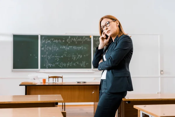 Beautiful pensive female teacher in formal wear and glasses in classroom — Stock Photo