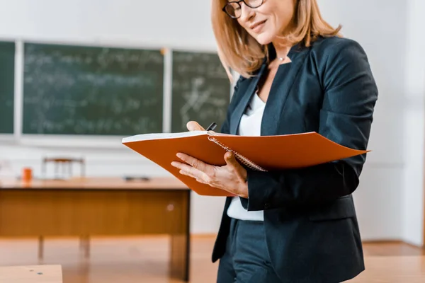 Vue recadrée de l'enseignante en tenue formelle écrivant dans un carnet de notes en classe — Photo de stock