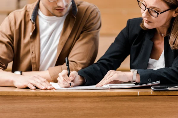 Vista recortada de la profesora comprobando los resultados del examen de estudiante masculino en el aula - foto de stock