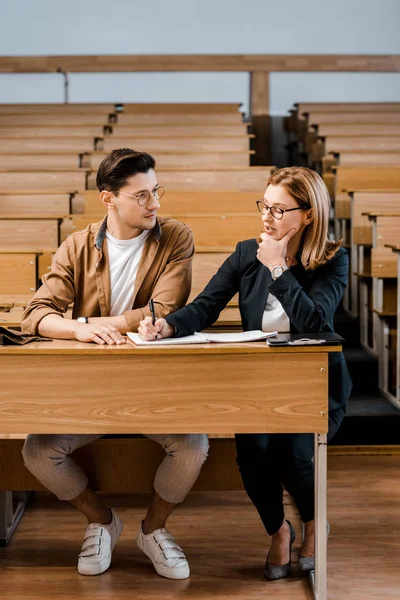Nachdenkliche Lehrerin berührt Kinn und überprüft Prüfungsergebnisse männlicher Schüler im Klassenzimmer — Stockfoto