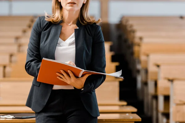 Visión parcial de la profesora universitaria sosteniendo el diario y escribiendo en el aula - foto de stock