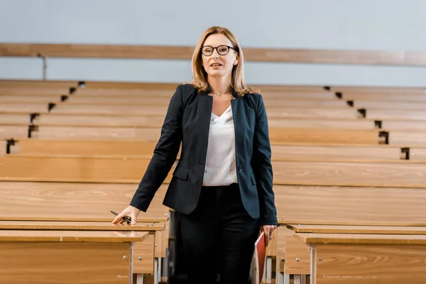 Professeure d'université en lunettes tenant un journal et un stylo en classe — Photo de stock