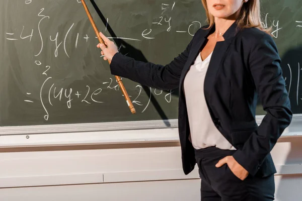 Vista ritagliata di insegnante donna con puntatore in legno che spiega equazioni matematiche in classe — Foto stock