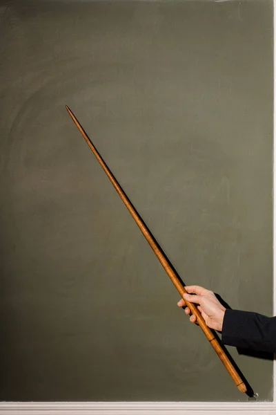 Cropped view of female teacher holding wooden pointer on chalkboard background — Stock Photo