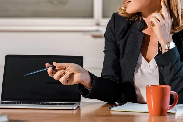 Cropped view of teacher sitting at desk and pointing at laptop with blank screen — Stock Photo