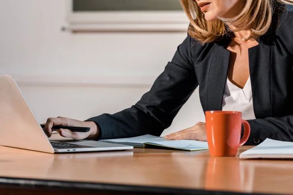 Vista ritagliata dell'insegnante utilizzando il computer portatile e seduto alla scrivania — Foto stock