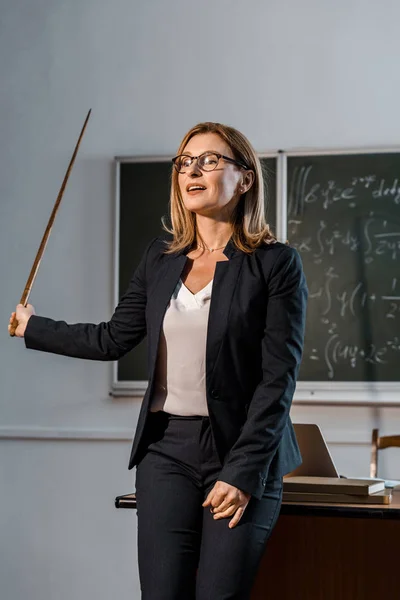 Professora com ponteiro de madeira explicando equações matemáticas em sala de aula — Fotografia de Stock