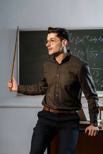 Maestro masculino en ropa formal y gafas sosteniendo puntero de madera y explicando ecuaciones en clase - foto de stock