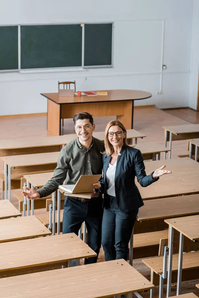 Felice studente maschio e insegnante femminile con le mani tese che tengono libri universitari in classe — Foto stock