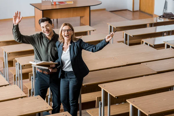 Alegre estudiante y profesora con las manos extendidas sosteniendo libros universitarios en el aula — Stock Photo