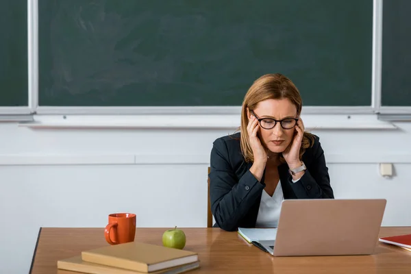 Lehrerin sitzt am Computertisch und hat Kopfschmerzen im Unterricht — Stockfoto