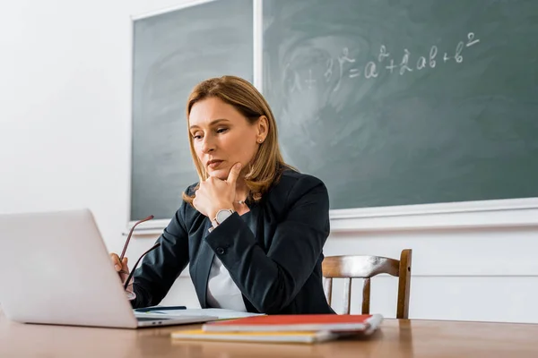 Женщина-учитель сидит за столом и за компьютером во время урока в классе — стоковое фото